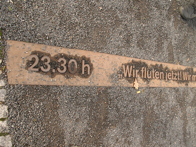 I gruset på den historiske plads viser denne tidslinje, at Muren blev åbnet kl. 23.30. "Wir fluten jetzt" betyder i fri oversættelse: Vi slipper floden løs. Citat fra en grænsesoldat om den flodbølge af berlinere, der pressede på for at få portene åbnet til Vestberlin. 